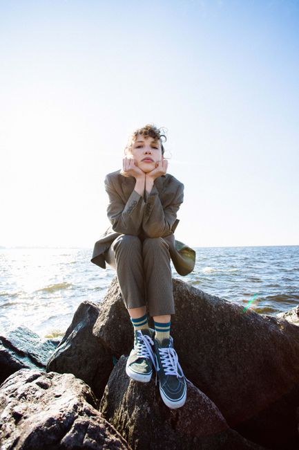 Stylish woman in suit sitting on rocks at the beach with ocean backdrop.