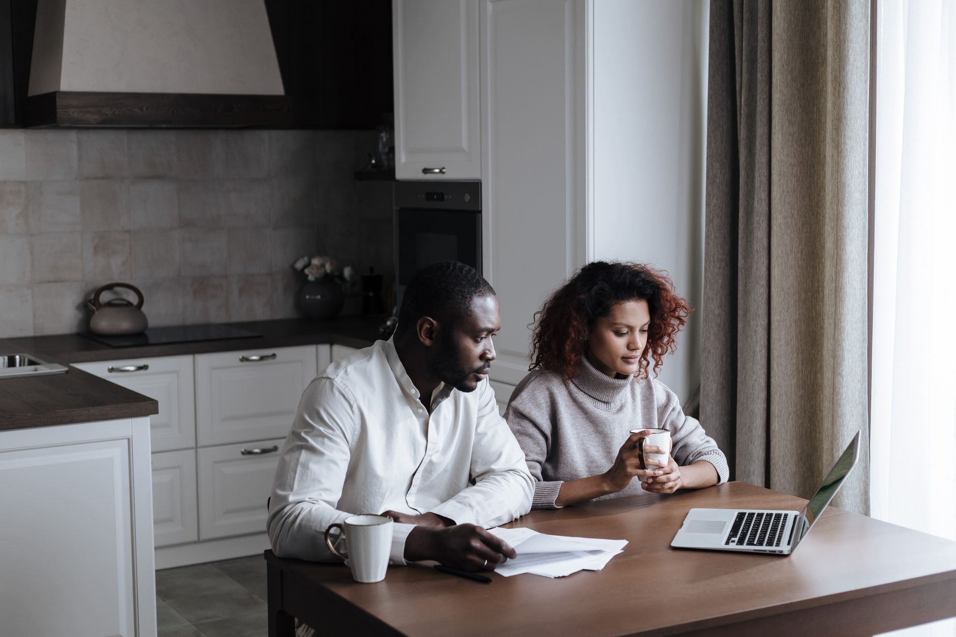 An executive couple sitting at a sunlit kitchen island working on laptops and reviewing calendar schedules.