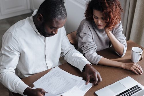 Free A couple reviews important documents together at a home desk with a laptop. Stock Photo