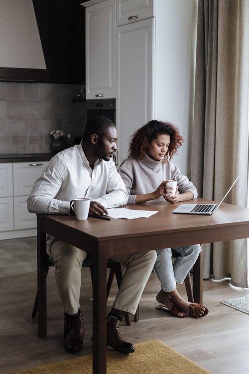 Free African American couple collaborating on a laptop in a modern kitchen setting at home. Stock Photo