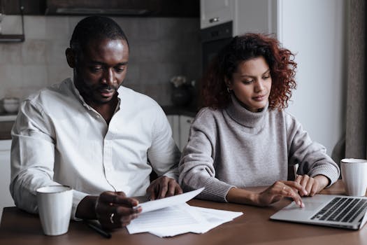 A diverse couple collaborates on a laptop at their home, handling documents over coffee.