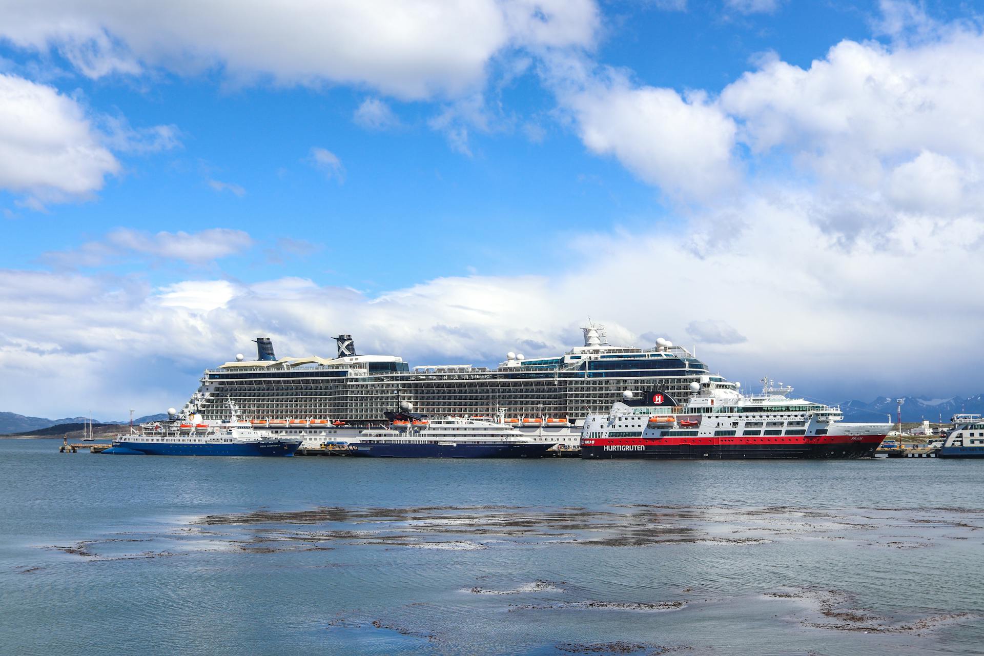 Cruise ships docked in the scenic Ushuaia Harbor on a cloudy day, with mountains in the background.