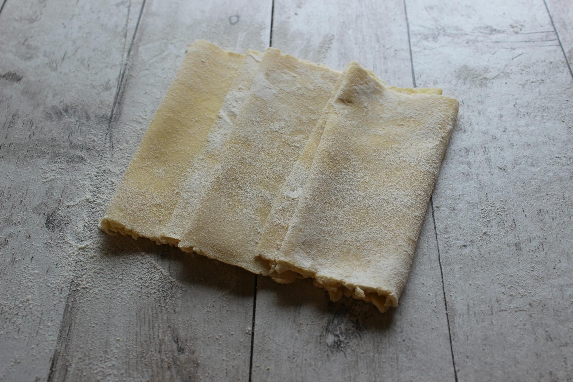 Close-up of freshly prepared pasta dough sheets on a rustic wooden surface, highlighting texture.