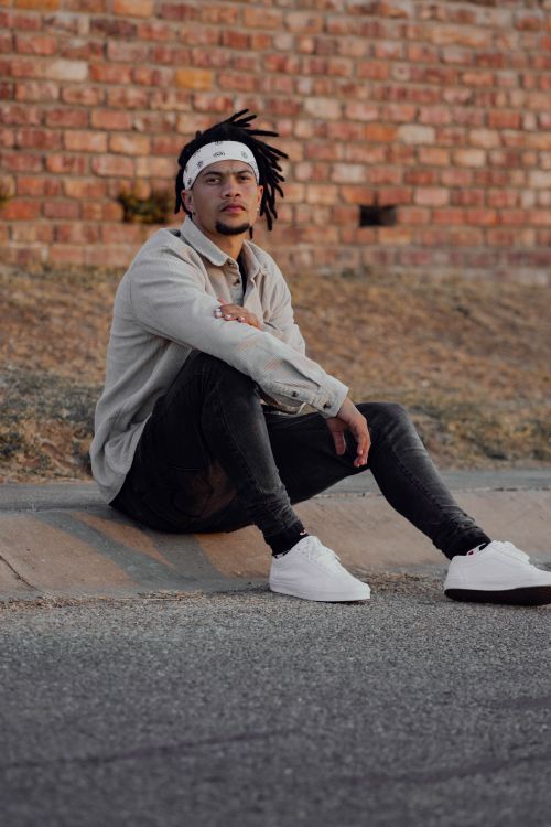 Free A fashionable bearded man with dreadlocks sitting on a curb, exuding style in Kariega, South Africa. Stock Photo