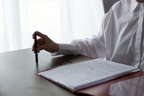 Unrecognizable Hand of Woman Sitting at Table and Reviewing Documents