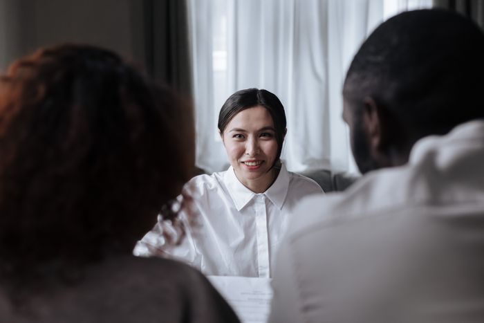 A woman in a white shirt smiling during a meeting with a couple indoors