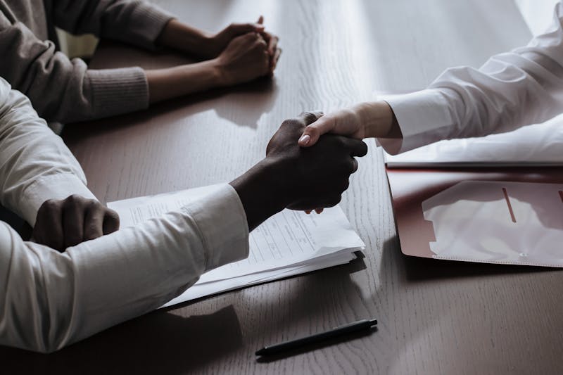 Two professionals shaking hands over a signed contract agreement on a desk