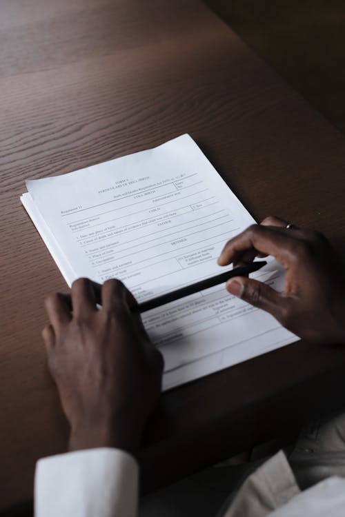 Hands Holding Pen with Documents Laying on Table