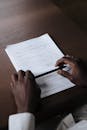 Hands Holding Pen with Documents Laying on Table