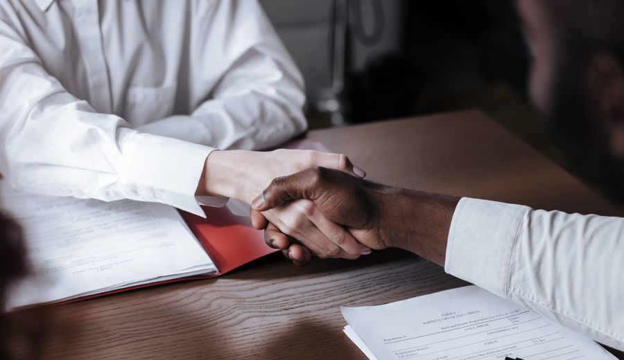 Two people shaking hands over documents, agreeing terms