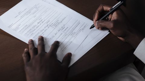 A detailed view of a man signing official documents with a pen at a table.