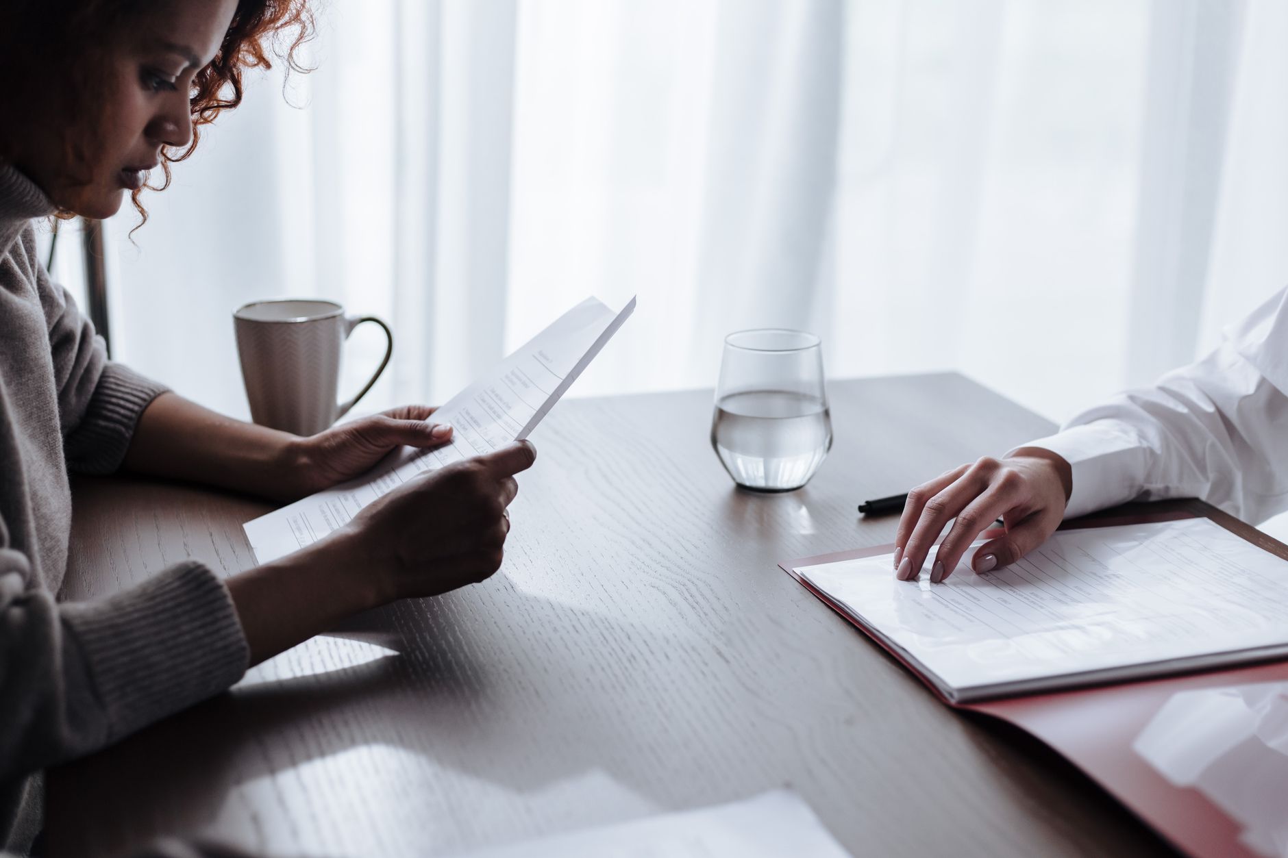 Two women reviewing documents with coffee and water on a table.