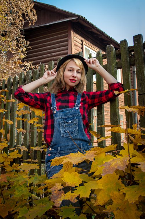 Free Stylish woman in autumn attire posing by a wooden fence surrounded by leaves. Stock Photo