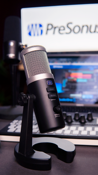 Close-up of a black microphone with audio equipment setup in a studio environment.