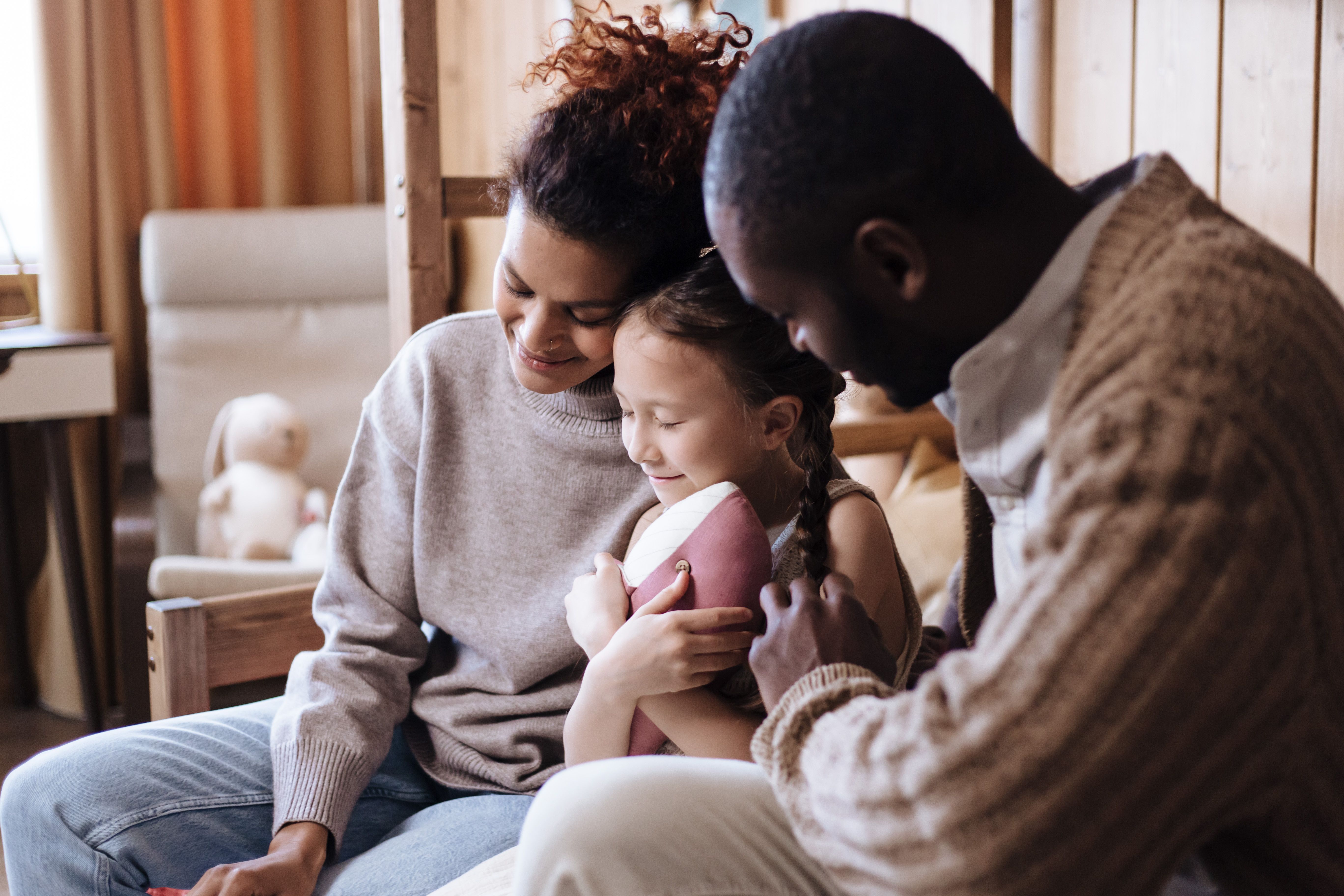 Family sitting close, embracing, in a cozy room.