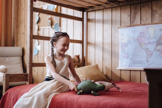 A young girl happily interacts with her toy dinosaur on a bed, in a warmly decorated room.
