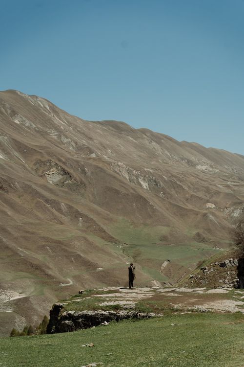 Free A lone figure stands on a vast mountain plateau under a clear sky, capturing solitude and nature's grandeur. Stock Photo