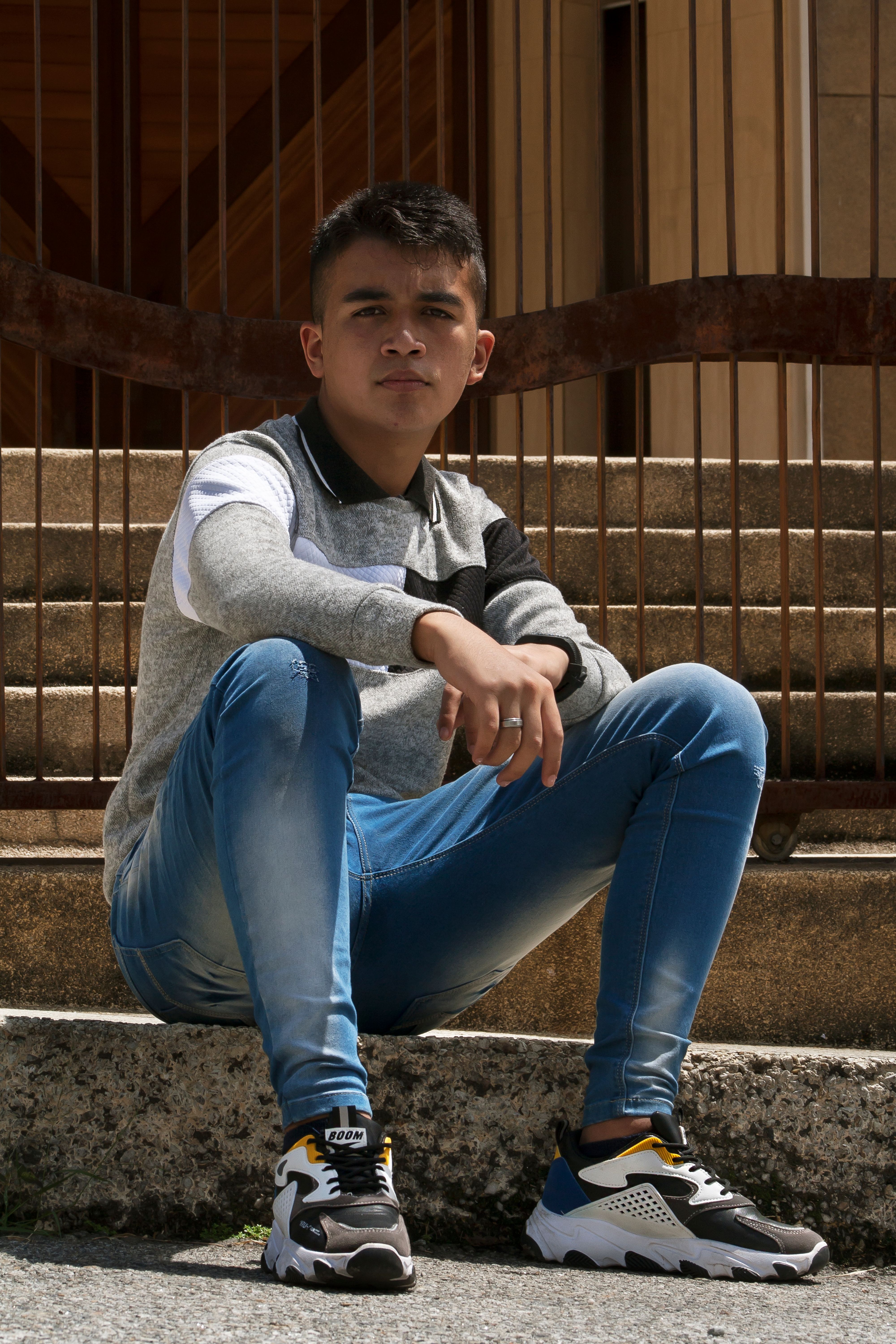 Casual portrait of a young man sitting on outdoor steps in Venezuela. His serious expression and modern clothing add depth to the shot.