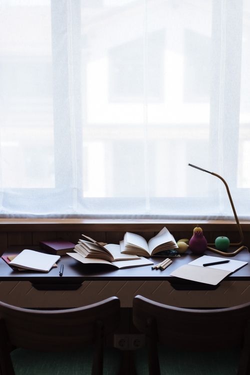 Free Tranquil study space with open books, pencils, and toys on a desk, soft daylight through the window. Stock Photo