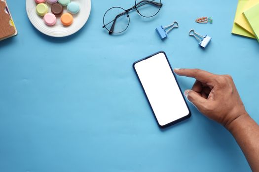 Flat lay smartphone mockup on blue surface with office supplies and macarons, perfect for tech or lifestyle themes.