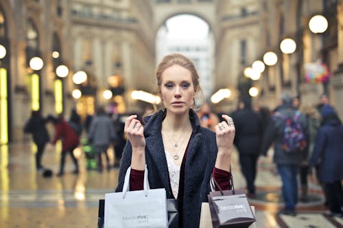 免费 女人穿着黑色大衣，拿着各种颜色的购物袋，在建筑物上 素材图片