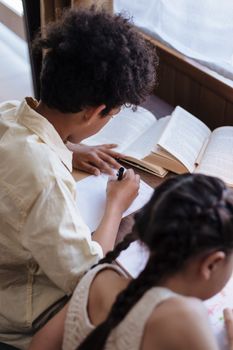 Two children draw and read together indoors, focusing on creative learning activities.
