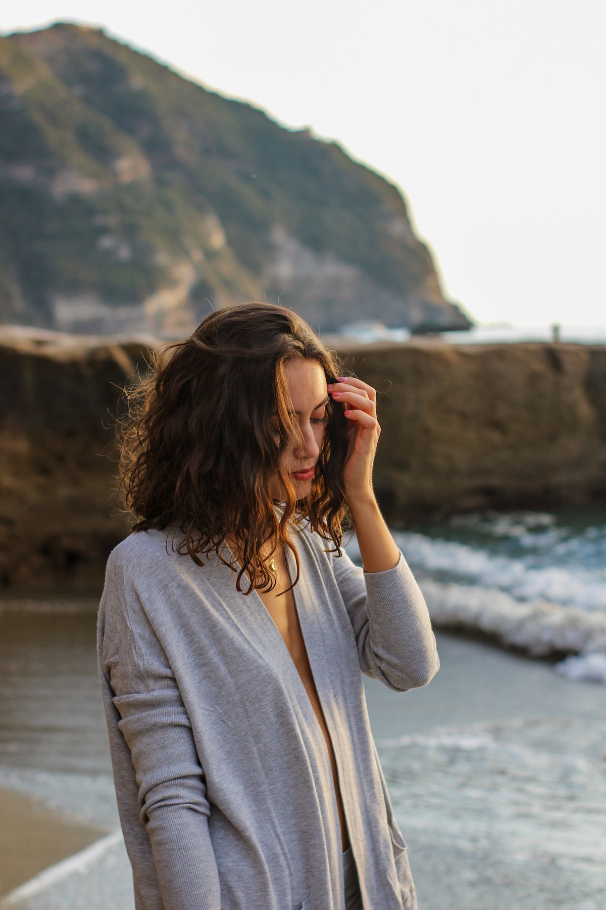 A woman on the beach in a fine knit touching her hair — the quietly luxurious summer knit