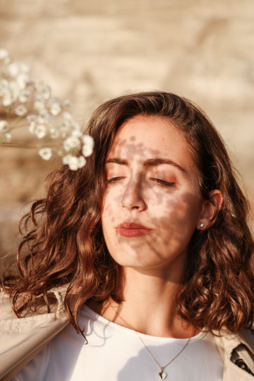 Free Portrait of a woman with wavy hair and floral shadow on her face, basking in sunlight. Stock Photo