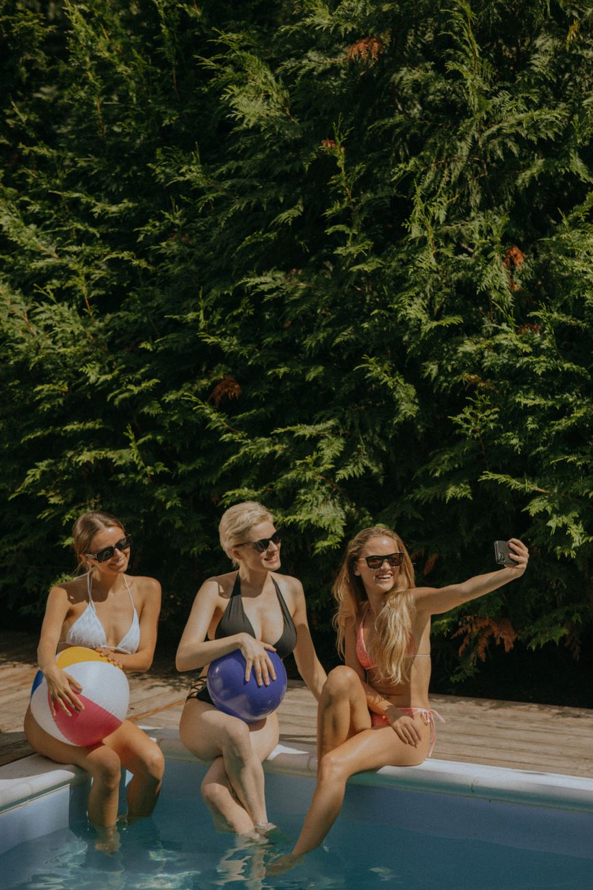 Three women in swimsuits taking a selfie by the pool, enjoying summer vibes.