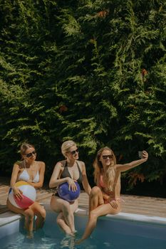 Three women in swimsuits taking a selfie by the pool, enjoying summer vibes.