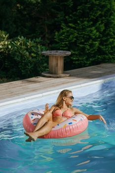 Woman in bikini floating on donut inflatable in sunny poolside setting.