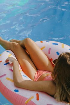 Woman in swimwear relaxing on a donut float in a swimming pool during sunny summer day.