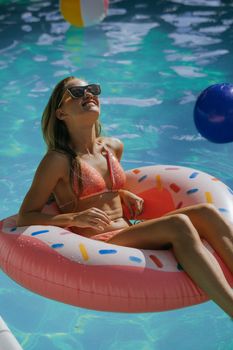 Young woman enjoying summer sun on inflatable donut in pool.
