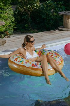 Woman enjoying a sunny day relaxing on a colorful inflatable donut in a swimming pool.