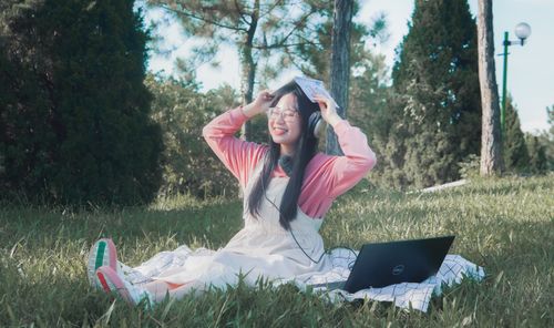 Free Smiling young woman enjoying time outdoors with a laptop and headphones. Stock Photo