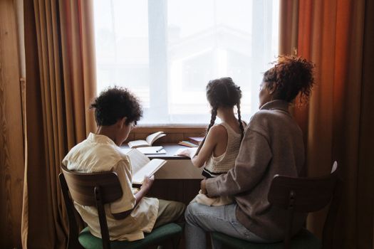 A family of three reads by a window, enjoying a quiet and educational moment indoors.