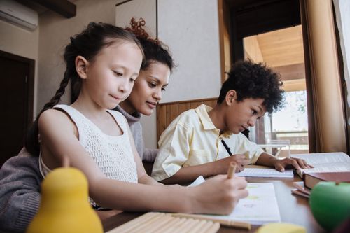 Free A caring mother helps her two children with homework in a cozy indoor setting. Stock Photo