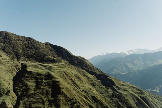 Explore the breathtaking green mountains under a clear blue sky with snow-capped peaks in the distance.