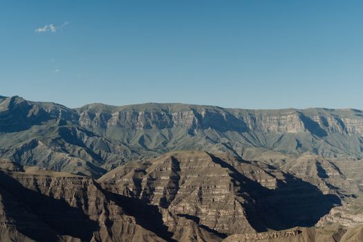 A stunning aerial shot showcasing Dagestan's majestic rocky mountains under a clear blue sky.