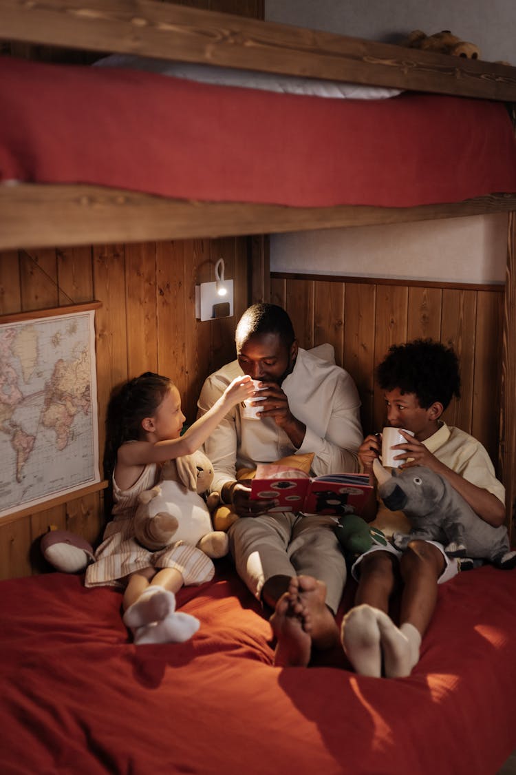 Father And His Kids Sitting On Bunk Bed Drinking