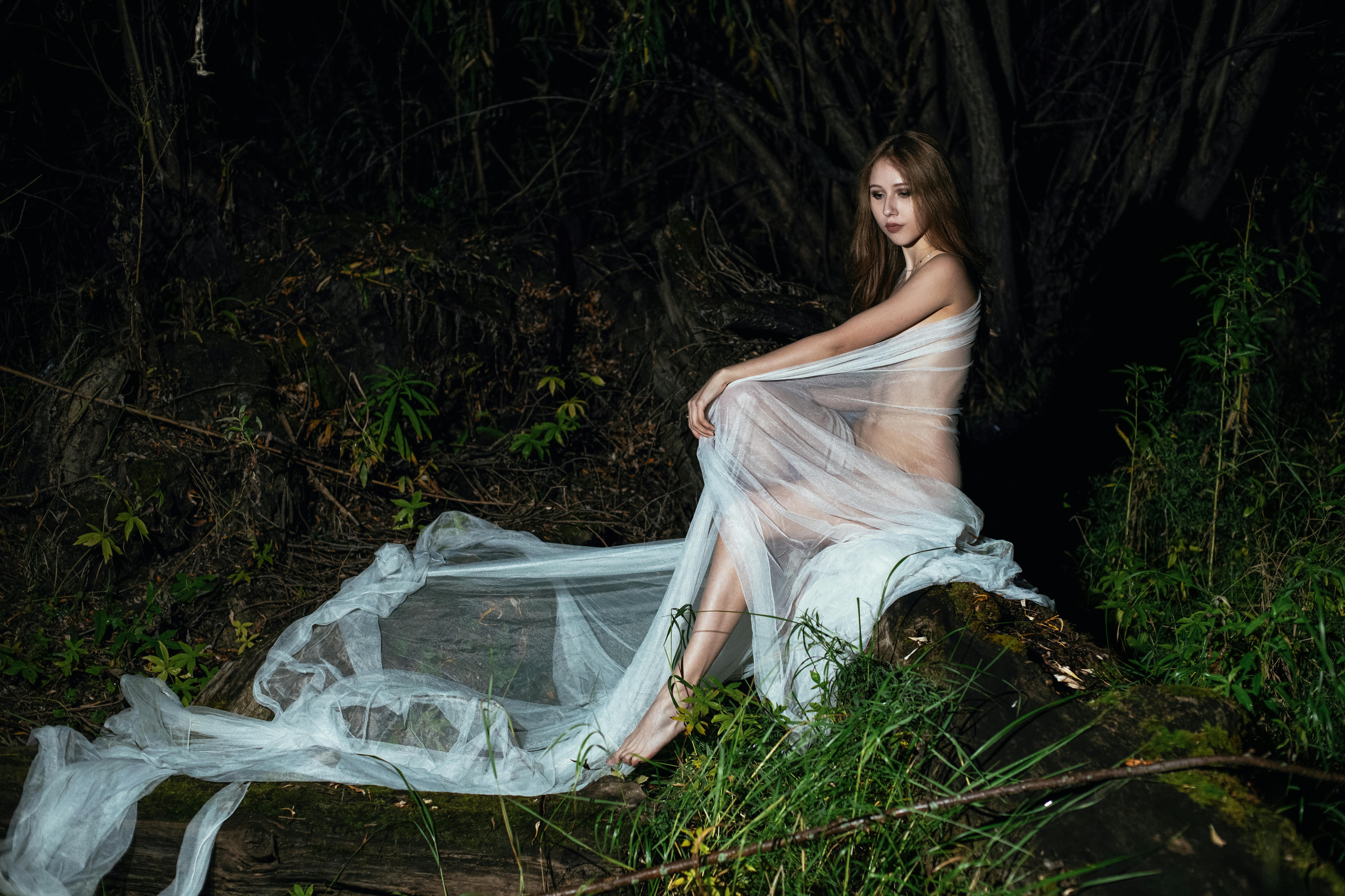 naked woman in white organza textile sitting in the forest