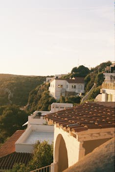 Charming cliffside houses with terracotta roofs overlooking a Mediterranean landscape at sunset.