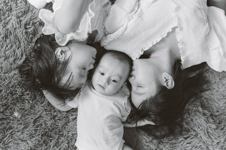 Grayscale Photo Of Woman And A Girl Kissing The Baby