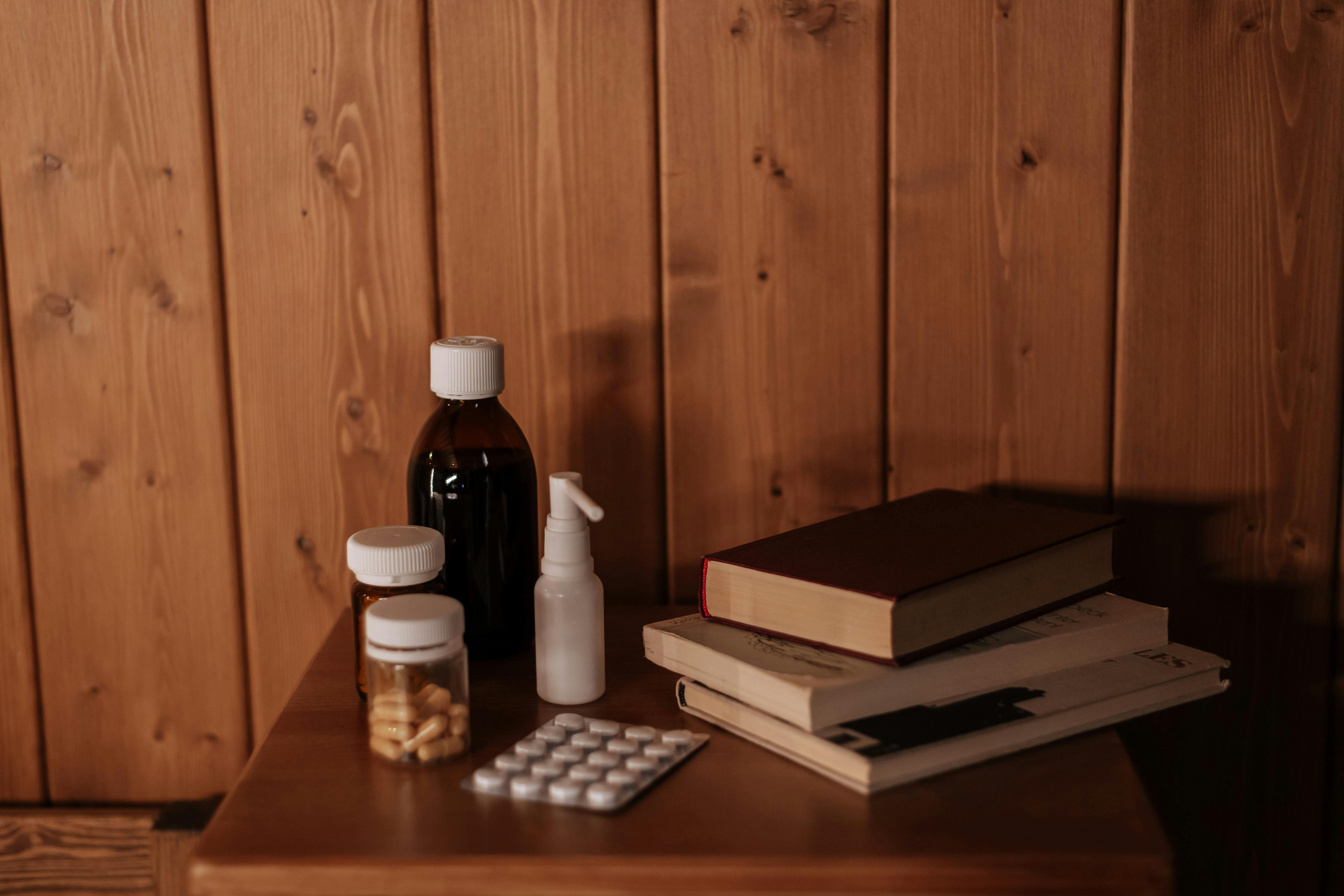 Free A cozy interior scene with medicines and books on a wooden bedside table, offering a warm and rustic ambiance. Stock Photo