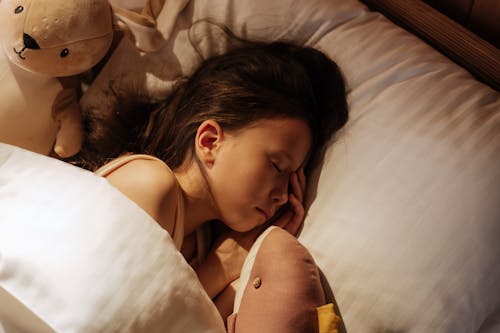 Free Girl Sleeping in Bed Between Cuddling Toys Stock Photo