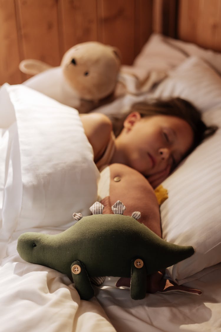 Girl Sleeping In Bed Surrounded By Plush Toys