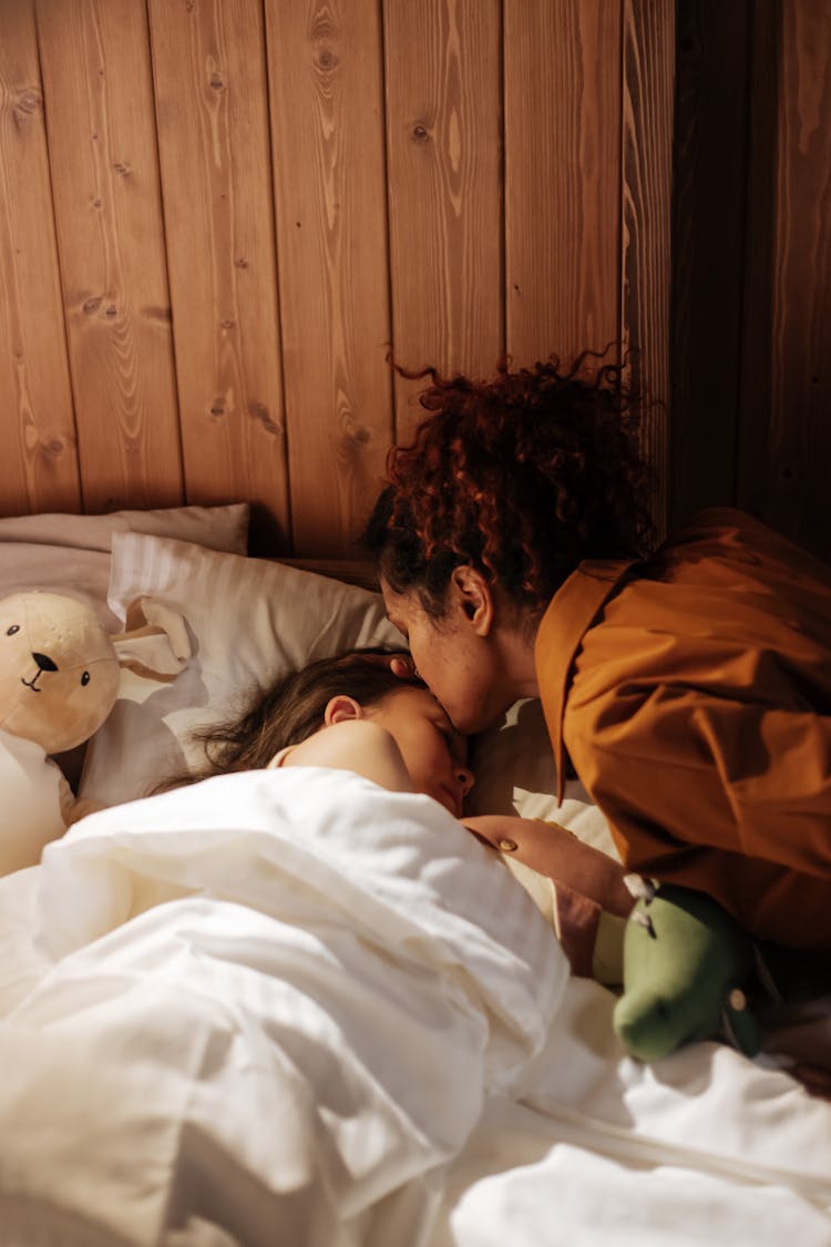 Mother Kissing Her Daughter In Bed For Goodnight 