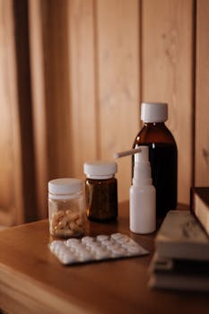Medical supplies including bottles, spray, and pills on a wooden table indoors with warm lighting.