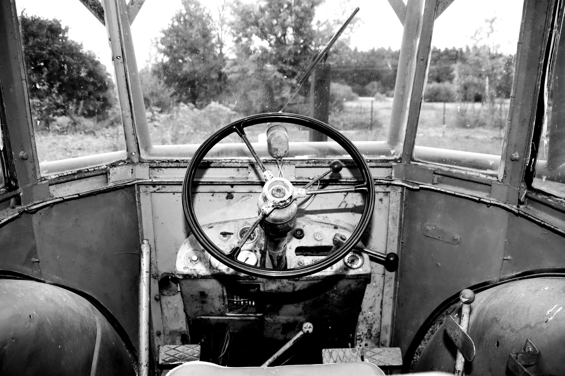 Black and white photo of a vintage tractor's interior featuring a round steering wheel.