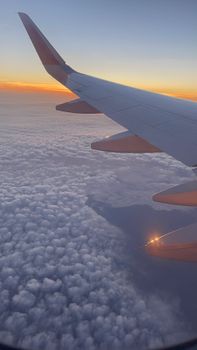 Airplane wing view showcasing vibrant sunset colors above the clouds. Captured mid-flight.